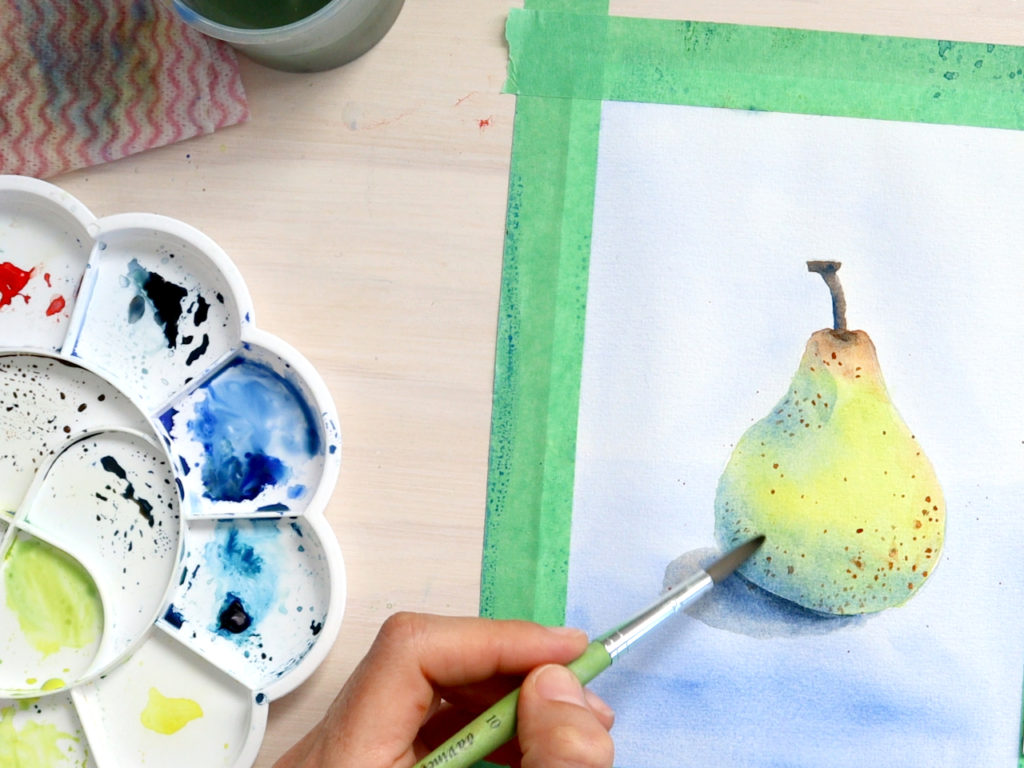 image of hand holding a brush painting a watercolour pear